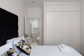 A hotel room with a bed, a black headboard, a white wardrobe, and a bathroom visible through an open door. - home.ly - London West End Apartments (London)