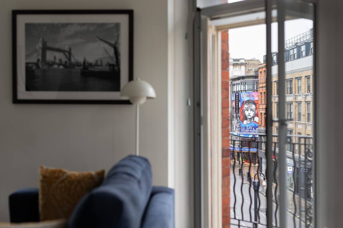 A living room with a sofa, a framed picture on the wall, and a view of a city street through a window.
