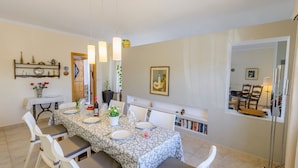 Un comedor con una mesa dispuesta para cuatro personas, sillas blancas, una estantería y una ventana con vistas.