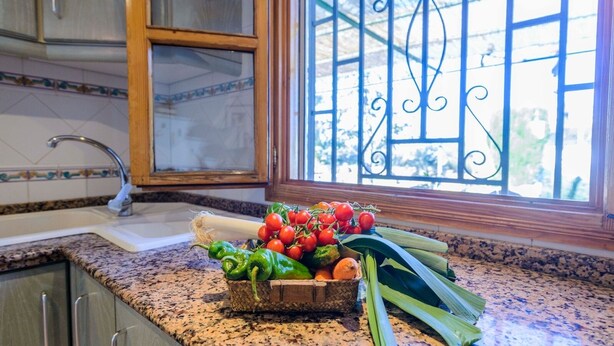 Una encimera de cocina con una cesta de verduras frescas, una ventana con rejas de hierro decorativas y un fregadero.