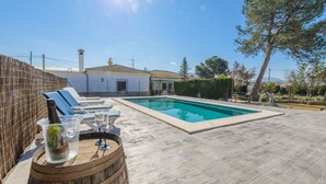 Una piscina con sillas de descanso y un barril de madera con una botella y vasos.