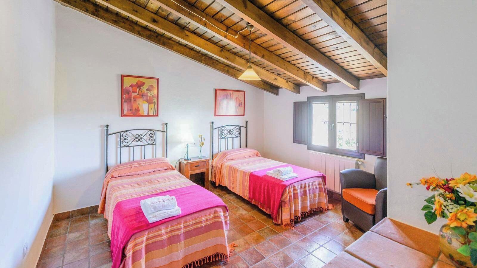 Una habitación con dos camas, una silla, una mesa y un ventanal.