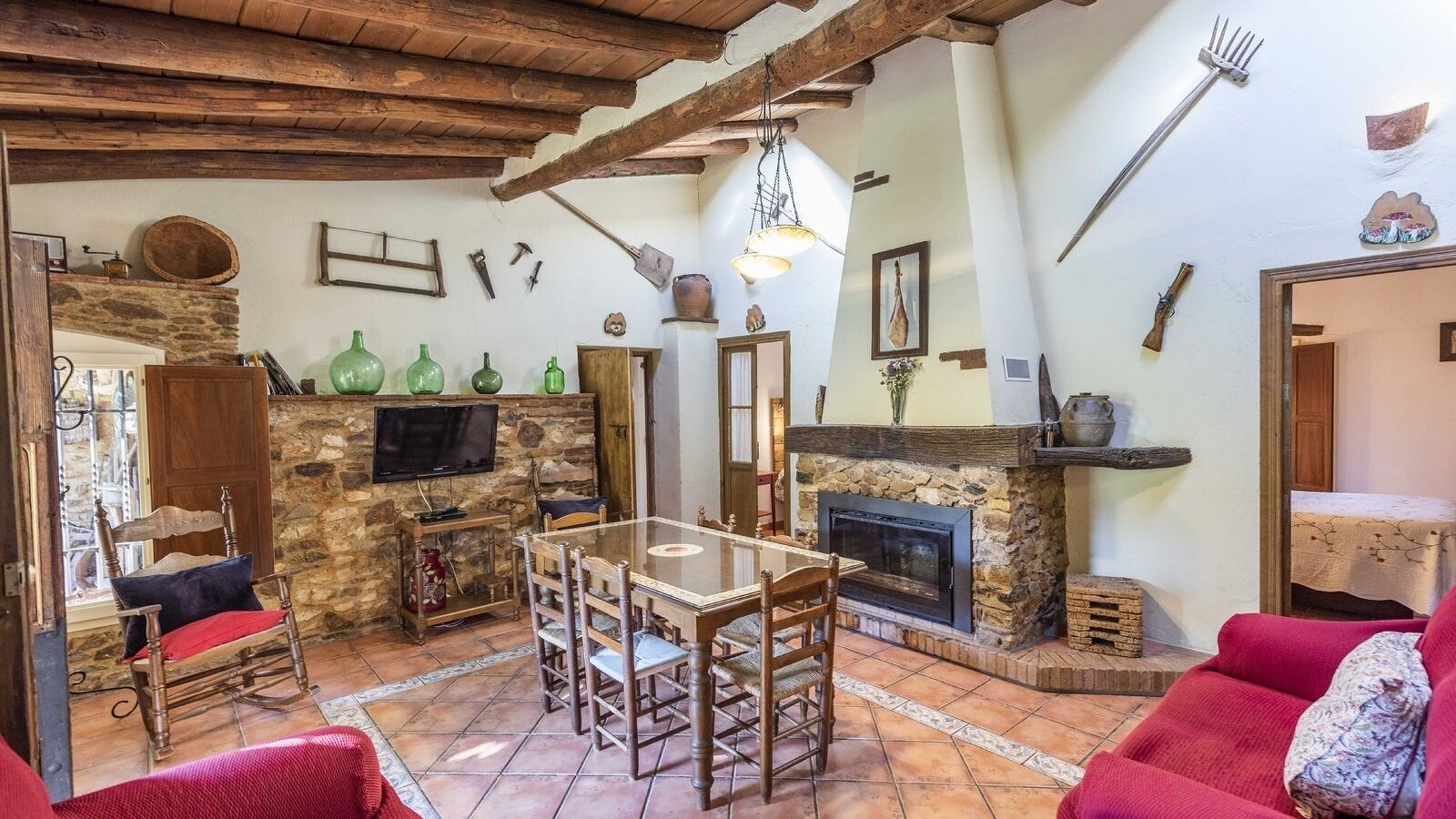 Un interior rústico con chimenea de piedra, muebles de madera y un televisor fijado a una pared de piedra.