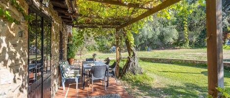 An outdoor patio with a table and chairs, a pergola, and a view of a grassy area with trees.