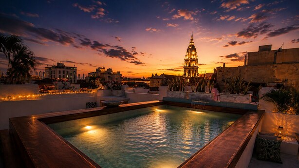Una piscina en la azotea con vistas a un paisaje urbano al atardecer, incluyendo un edificio destacado con cúpula.