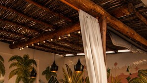 Una cocina con barra de madera, taburetes, lámparas colgantes y decoración tropical en la pared.