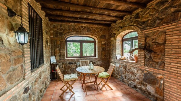 A rustic stone-walled room with a round wooden table and chairs, two arched windows, and a hanging lantern. - Casa Chantino Aracena by Ruralidays (Huelva)