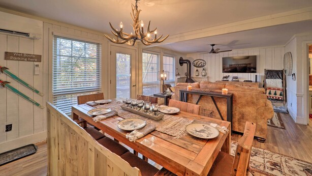 A dining area with a long wooden table set for four, a chandelier, and a kitchen in the background. - < 1 Mi to Beech Mtn Ski! Condo w/ Hot Tub Access (Beech Mountain)