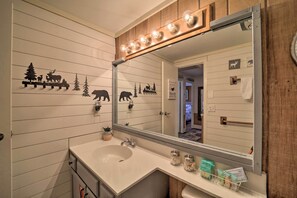 A bathroom with a white sink, wooden wall paneling, a mirror with lights, and animal-themed decorations. - < 1 Mi to Beech Mtn Ski! Condo w/ Hot Tub Access (Beech Mountain)