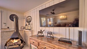 A cozy living room with a wood-burning stove, a mounted flat-screen TV, and decorative animal figurines on a wooden cabinet. - < 1 Mi to Beech Mtn Ski! Condo w/ Hot Tub Access (Beech Mountain)