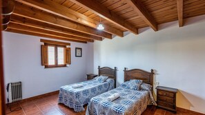 A bedroom with two beds, wooden beams on the ceiling, a window, and a radiator. - La Solana de Aracena by Ruralidays (Huelva)