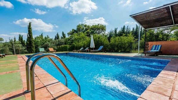 A rectangular swimming pool with a metal ladder on the left, surrounded by a tiled deck. There are lounge chairs and a covered area in the background. - La Solana de Aracena by Ruralidays (Huelva)