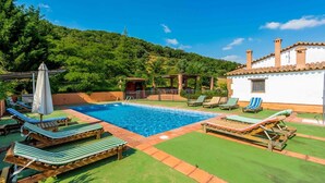 Piscina com espreguiçadeiras e um edifício branco com telhado em azulejo.