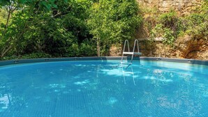 Ein klares, blaues Schwimmbecken mit einer Metallleiter, umgeben von üppiger Vegetation und einer felsigen Klippe.