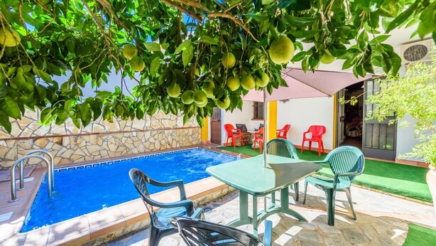 Una piscina con un muro de piedra y un borde empinado de baldosas, rodeada de mobiliario exterior y un muro de piedra.