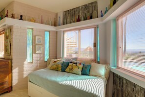 Cozy bedroom with a large bed, wooden dresser, and nightstand, featuring a window with blinds and a shelf with decorative vases.