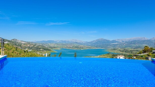 Une magnifique piscine à débordement d’un bleu profond, donnant sur un lac avec des montagnes en toile de fond.