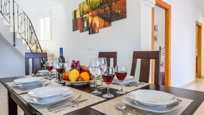 Une table à manger dressée avec des assiettes, des couverts, des verres et un saladier de fruits.