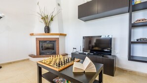 Un salon avec une cheminée, un téléviseur, un jeu d’échecs et une bibliothèque.