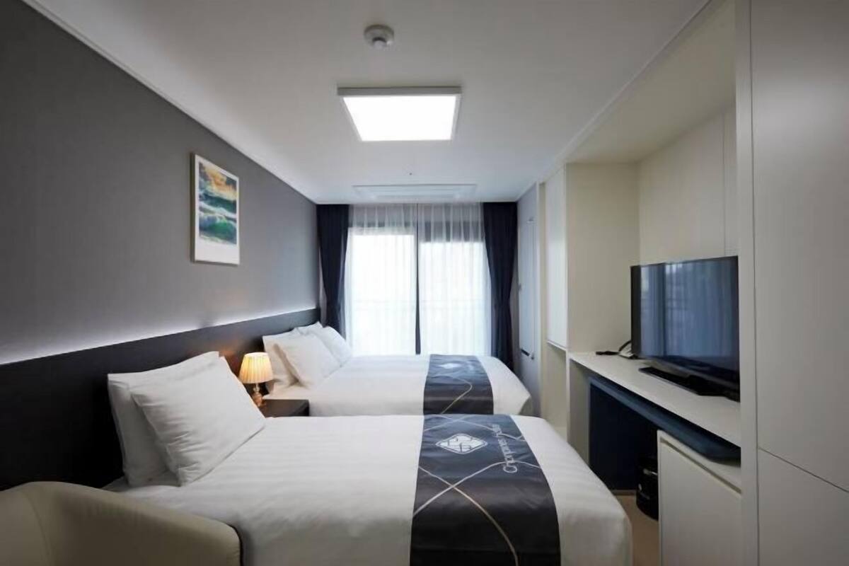 Habitació d'hotel amb dos llits, televisió i finestra amb cortines.
