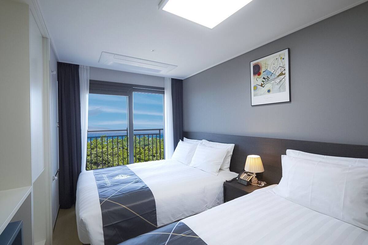 Habitació d'hotel amb dos llits, un finestral gran que dona a una vista, un quadre a la paret i una làmpada de nit.