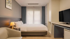 Et hotelværelse med en seng, et skrivebord med fjernsyn, en lampe og et billede på væggen.