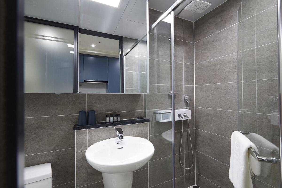 Un bany modern amb un box de dutxa de vidre, un lavabo blanc i un mirall sobre el lavabo.