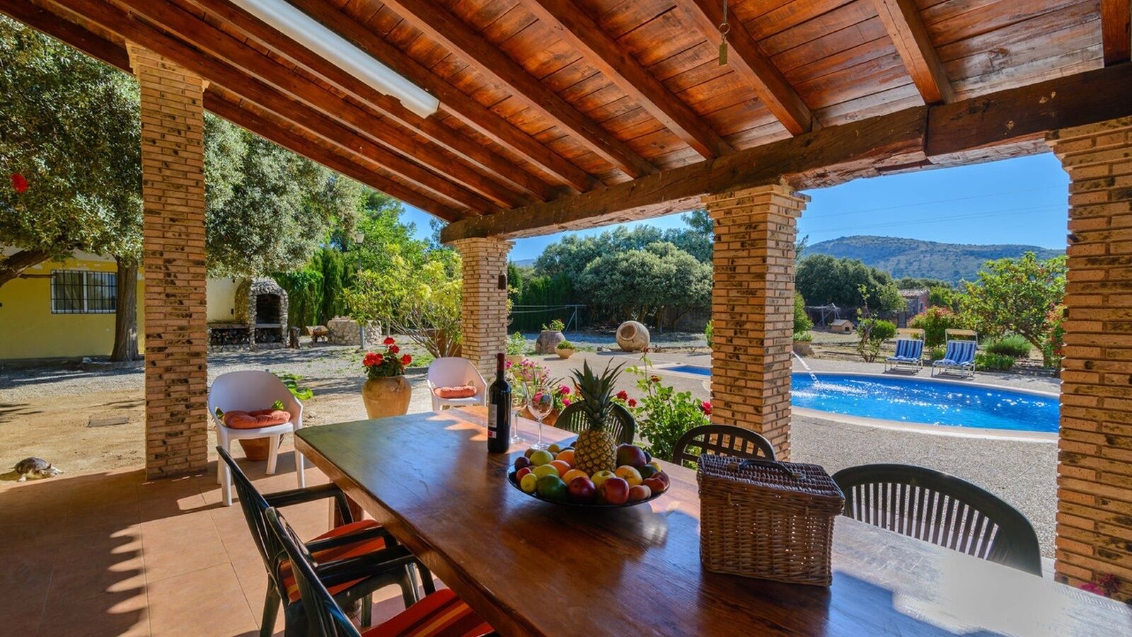 Une terrasse extérieure avec une table en bois, des chaises et une piscine en arrière-plan.