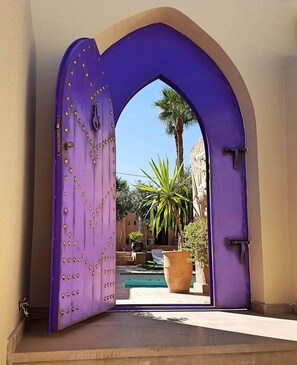 Un arco morado da acceso a un patio con piscina y plantas en macetas.