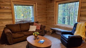 Un interior de cabaña acogedor, con un sofá de cuero marrón, una mesa de centro de madera con un libro y un banco.