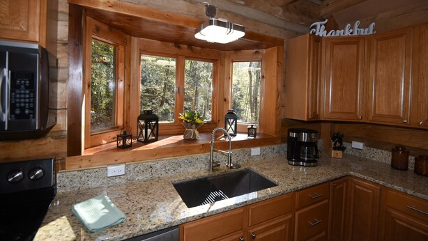 Una cocina con armarios de madera, un lavamanos de acero inoxidable, una cafetera y una ventana con vistas a árboles.