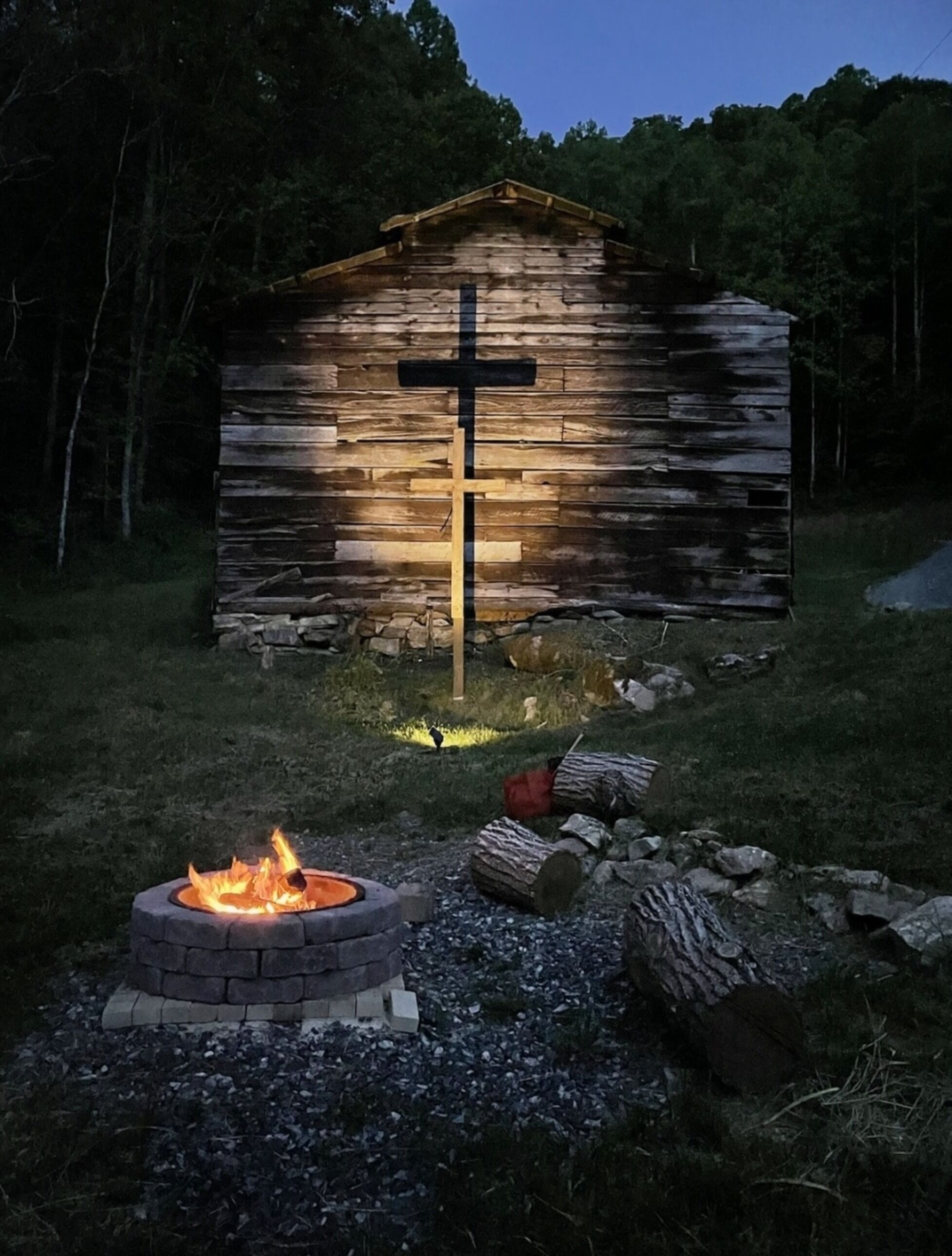 A rustic wooden cabin with a cross illuminated in front.