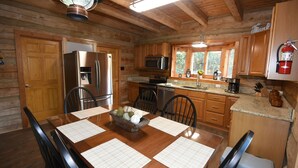 Cocina de cabaña de madera con una mesa de comedor, sillas, refrigerador, microondas, horno y extintor.
