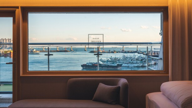 A room with a large window overlooking a harbor, a sign reading "DO NOT LEAN," and a view of boats and a bridge. - Nampo Ocean 2 Heaven Hotel&Spa (Busan)