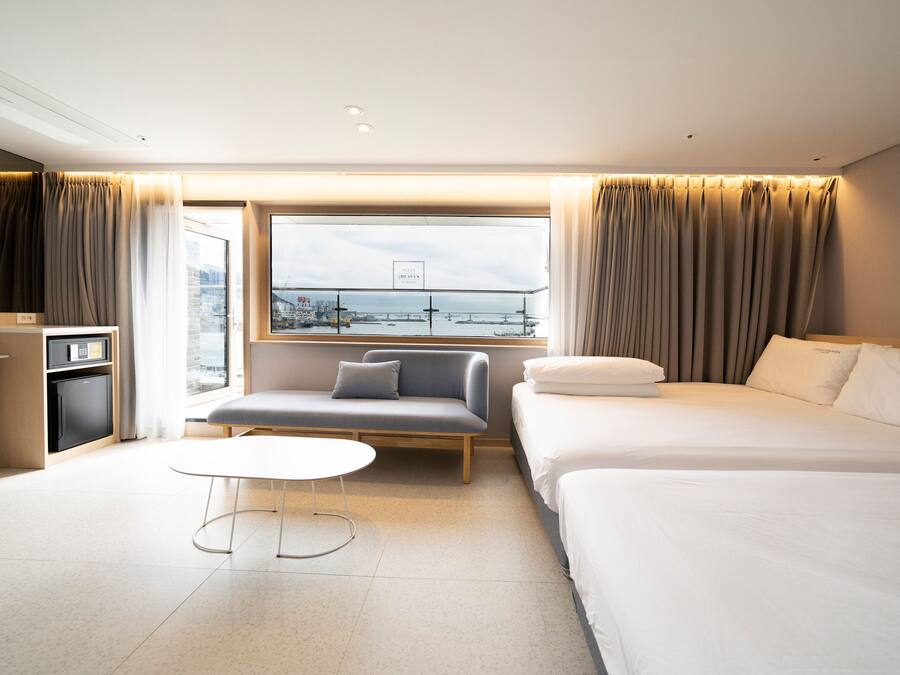 Habitación de hotel con cama, sofá, escritorio, silla y ventana con vista a la ciudad.