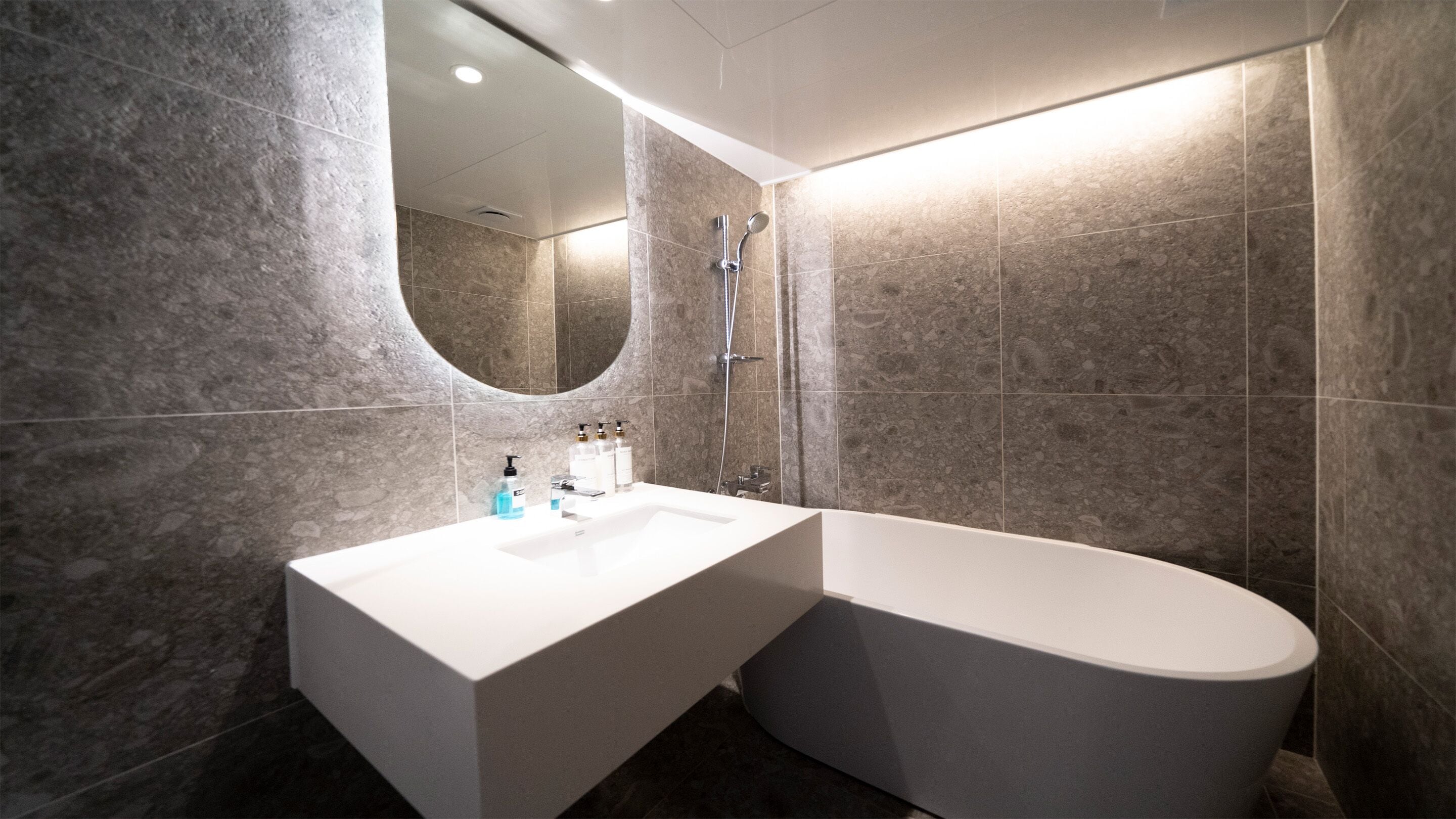 A modern bathroom with a freestanding bathtub, a large mirror, and a vanity with toiletries.