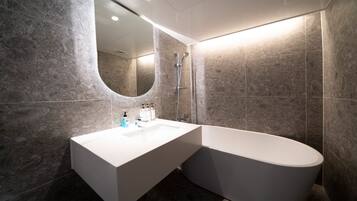 A modern bathroom with a freestanding bathtub, a large mirror, and a vanity with toiletries.