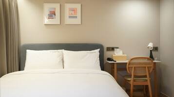 A hotel room with a bed, a desk with a chair, a lamp, a phone, and two framed pictures on the wall.