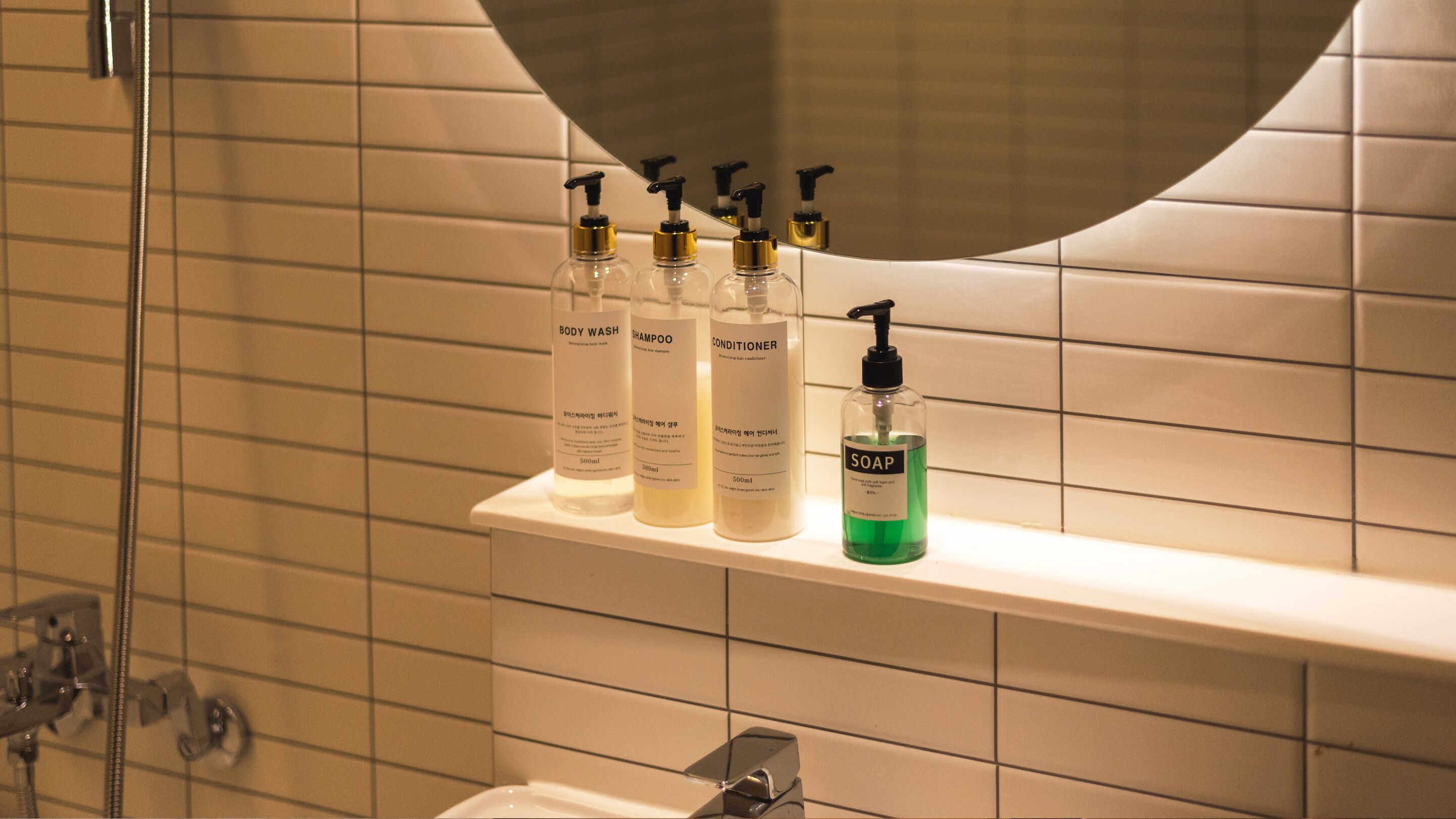 Une salle de bain avec une étagère où sont rangés des flacons de gel douche, de shampoing, d’après-shampoing et de savon.