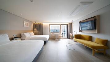A hotel room with two beds, a sofa, a TV, and a view of the city.