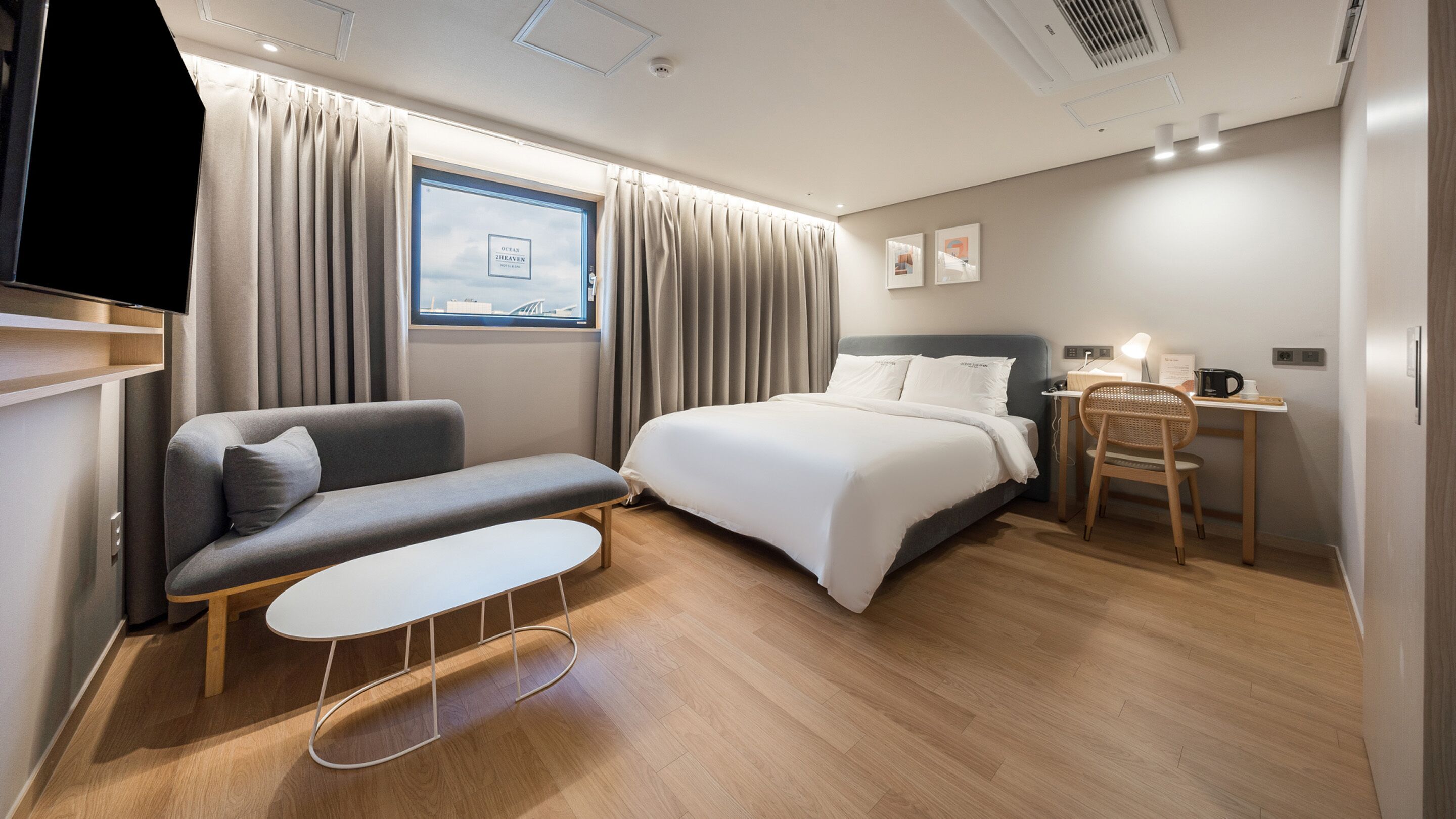A modern hotel room with a bed, a sofa, a small table, and a desk with a chair.