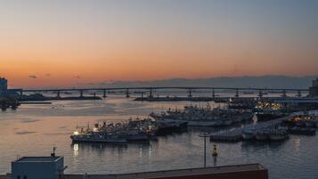 A harbor at sunset with multiple boats docked, a bridge in the background, and industrial buildings.