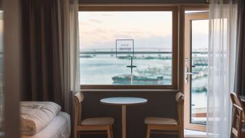 A hotel room with a bed, a small table, two chairs, and a view of the ocean through a window.