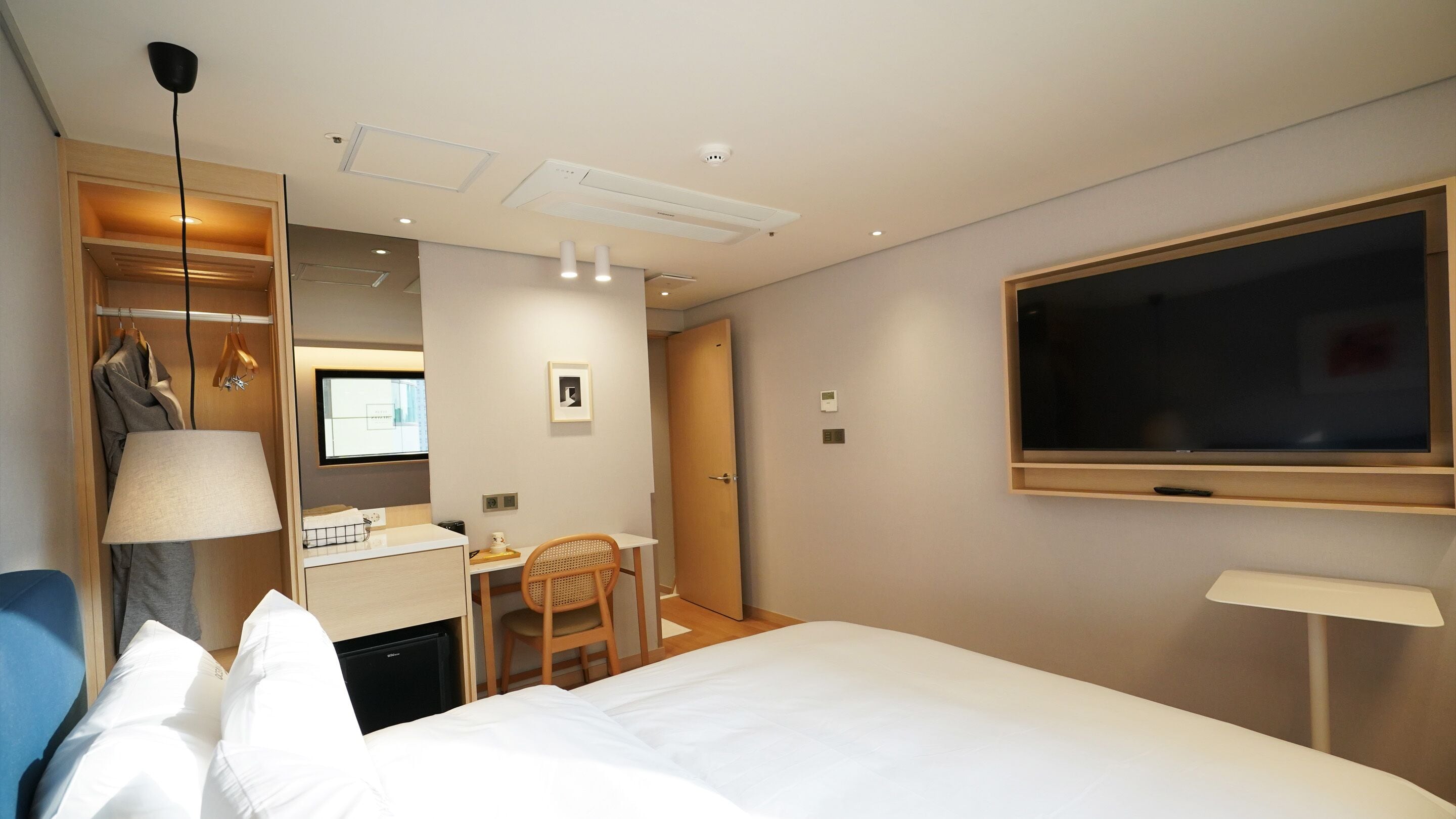 Una habitación de hotel con cama, escritorio, silla, televisor y armario.