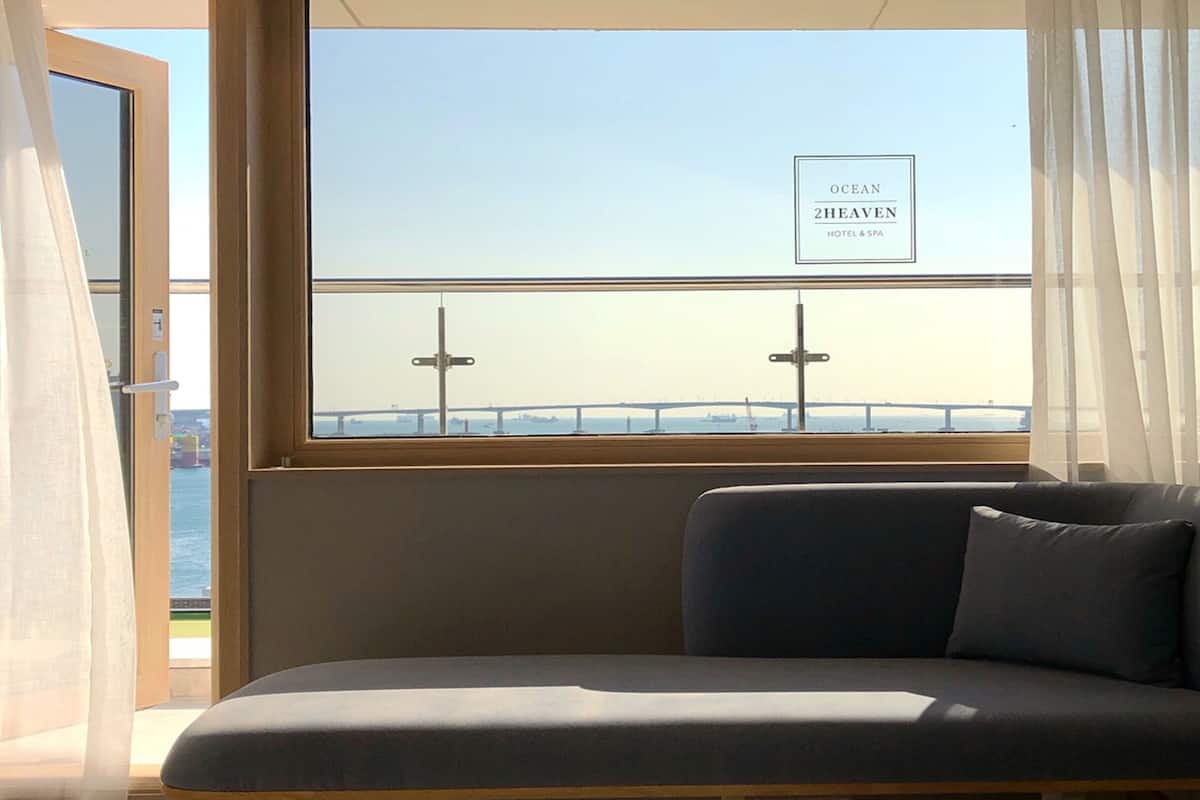 A room with a view of a bridge and the sea, a sofa, and a sign reading "OCEAN 2HEAVEN HOTEL & SPA".