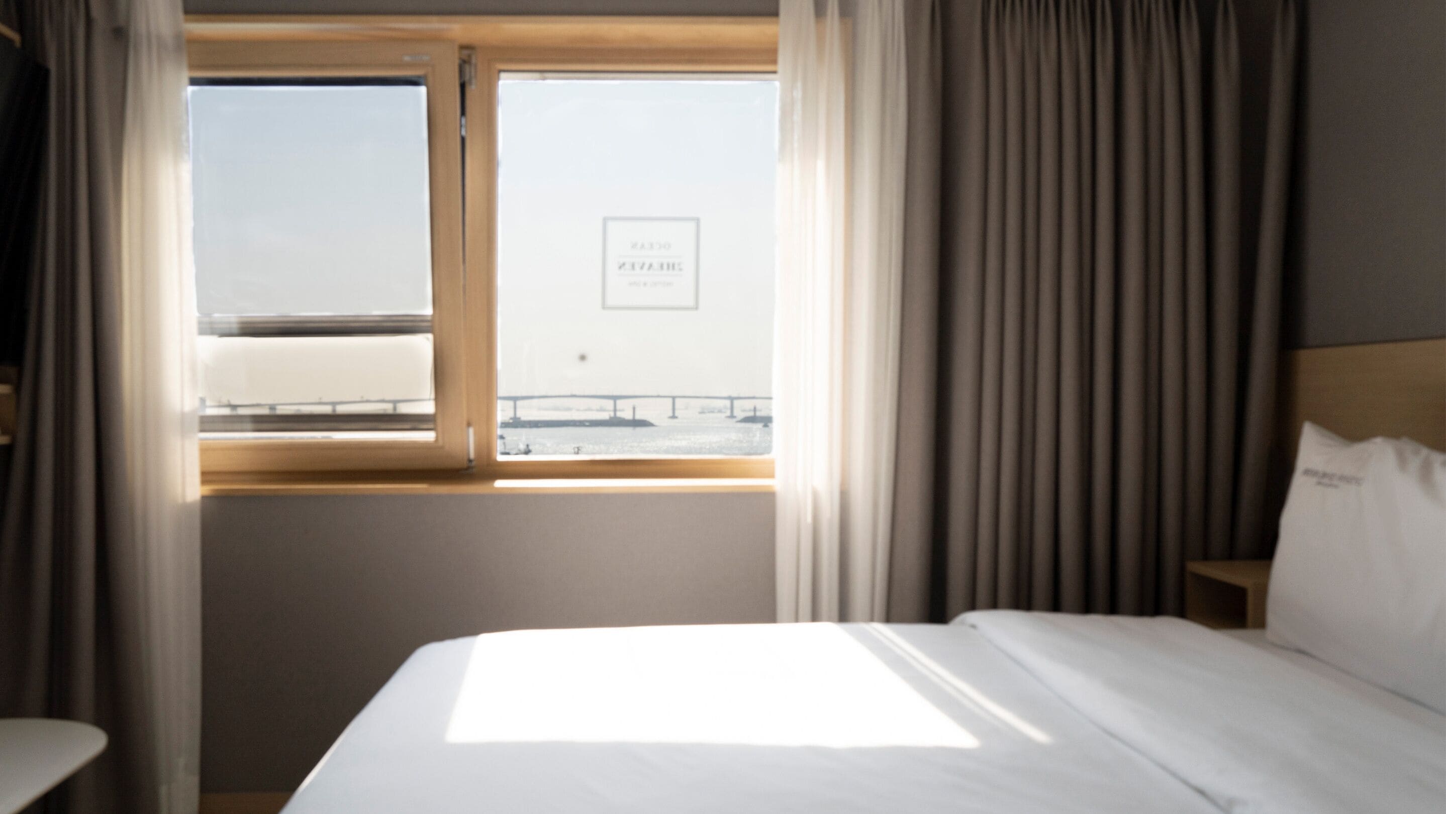 Une chambre d’hôtel avec un grand lit, une fenêtre donnant sur un pont et une pancarte sur la fenêtre.