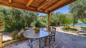 An outdoor patio with a round table and chairs, surrounded by stone walls and greenery.