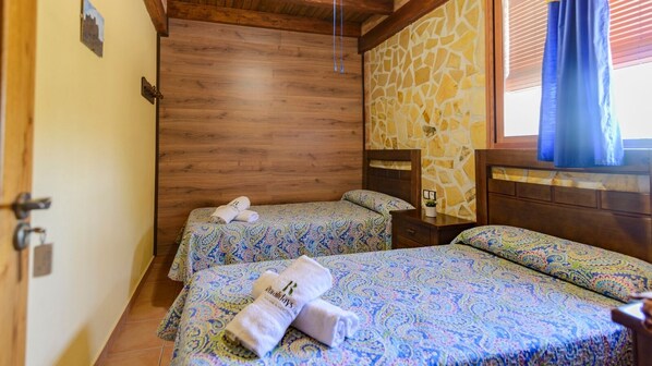 A room with two beds, wooden walls, a stone accent wall, and a window with blinds.