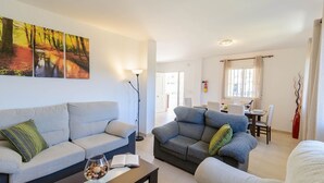 Sala de estar com dois sofás, uma mesa de centro e uma estante. Há uma área de jantar com mesa e cadeiras.