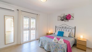 Quarto com cama, mesas de cabeceira, um espelho e janela com cortinas.